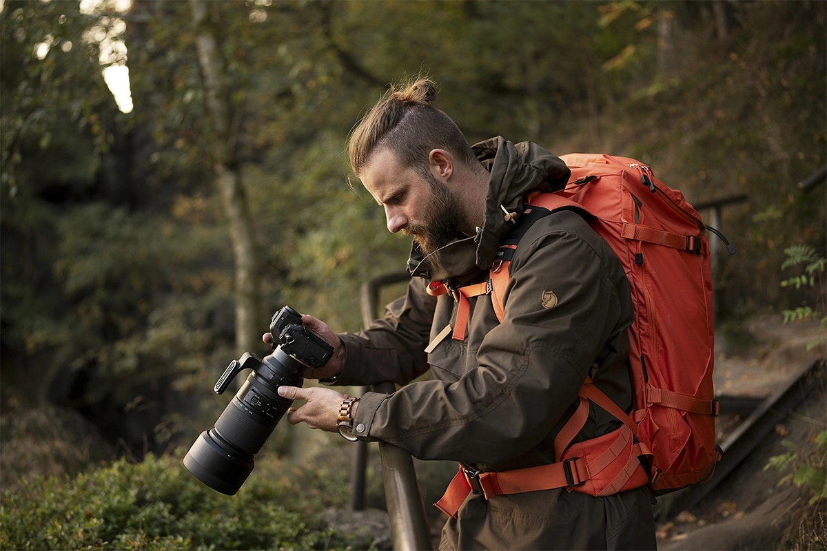 Fotógrafo ajustando un teleobjetivo zoom en un entorno natural al aire libre, en una demostración del uso práctico de la fotografía de vida silvestre.