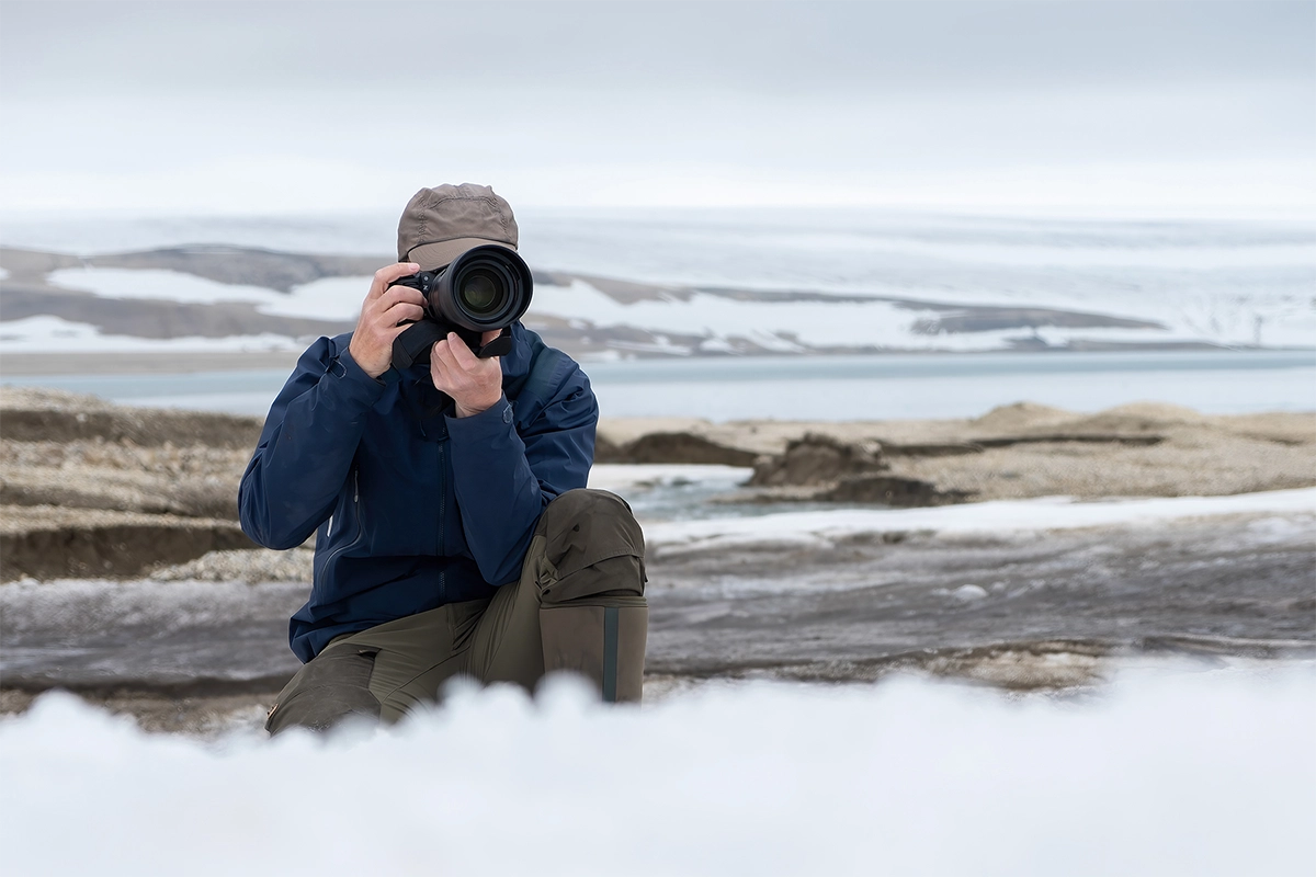 Wildlife photographer using a telephoto lens outdoors in a snowy landscape.
