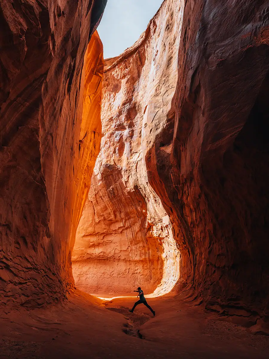 A person jumping over a crack in the canyon that looks like an hourglass.