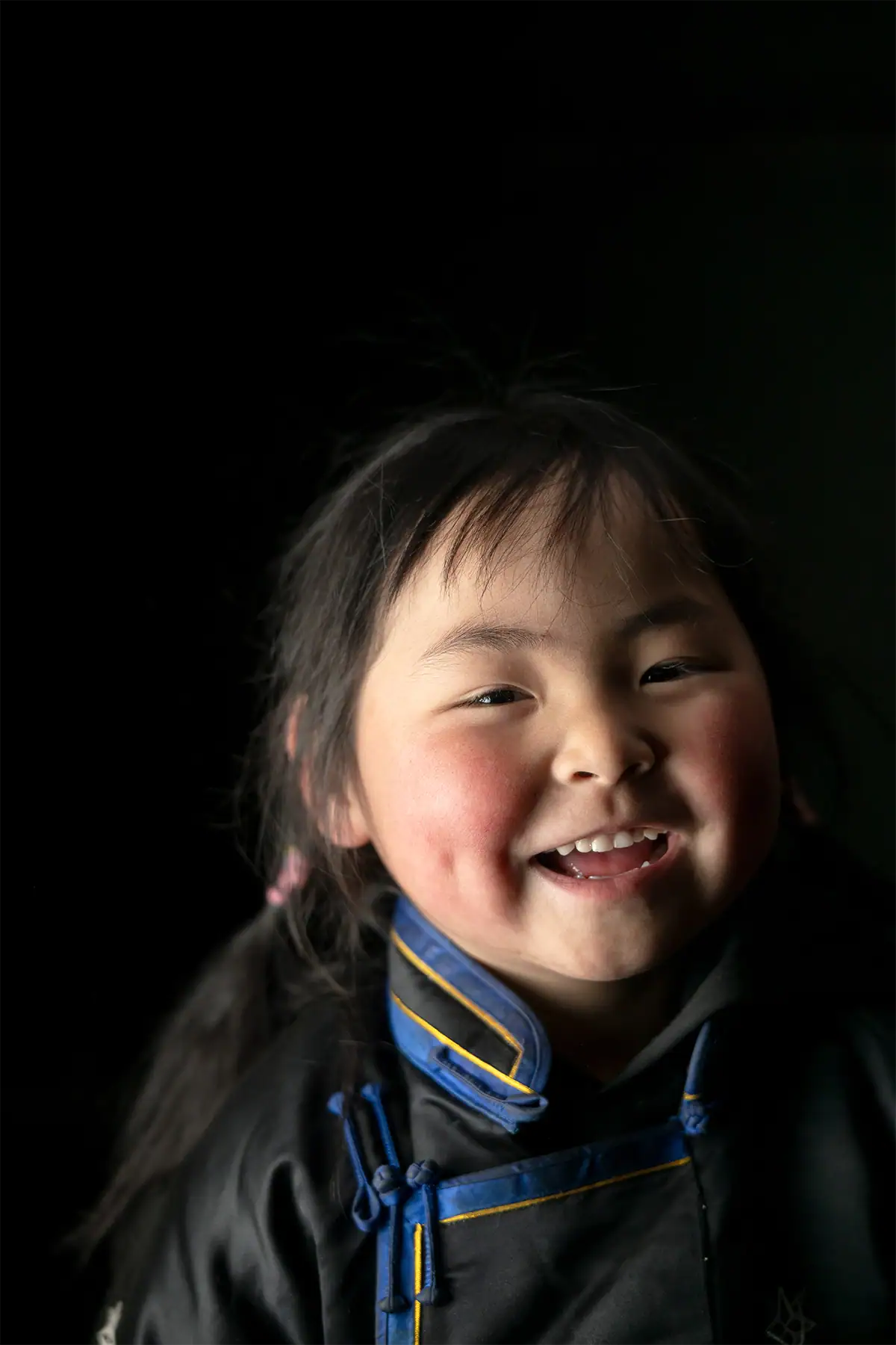 Telephoto portrait of a smiling child against a dark softly blurred background.