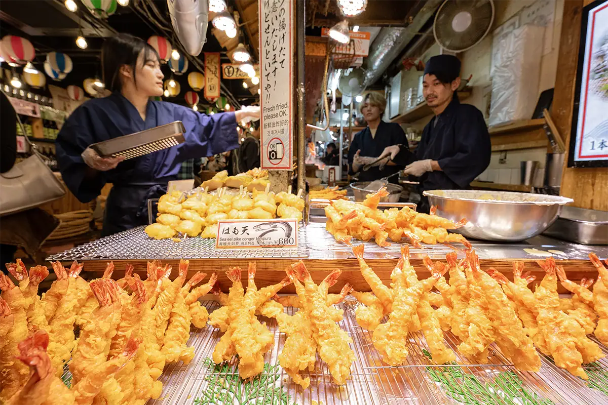 Wide-angle photo of tempura displayed close to the camera at a busy Japanese food stall.