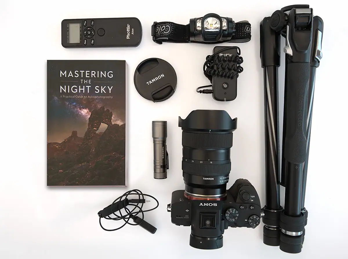 Astrophotography gear flat lay with camera, Tamron lens, tripod, remote release, headlamp, and accessories.