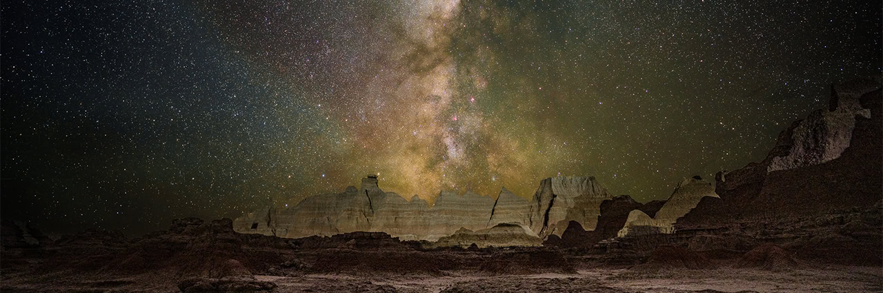 Milky Way stretching across a star-filled night sky above a desert landscape.