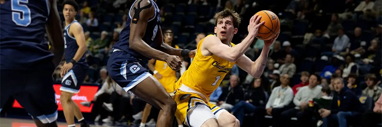 A basketball player drives toward the basket during fast indoor sports action.