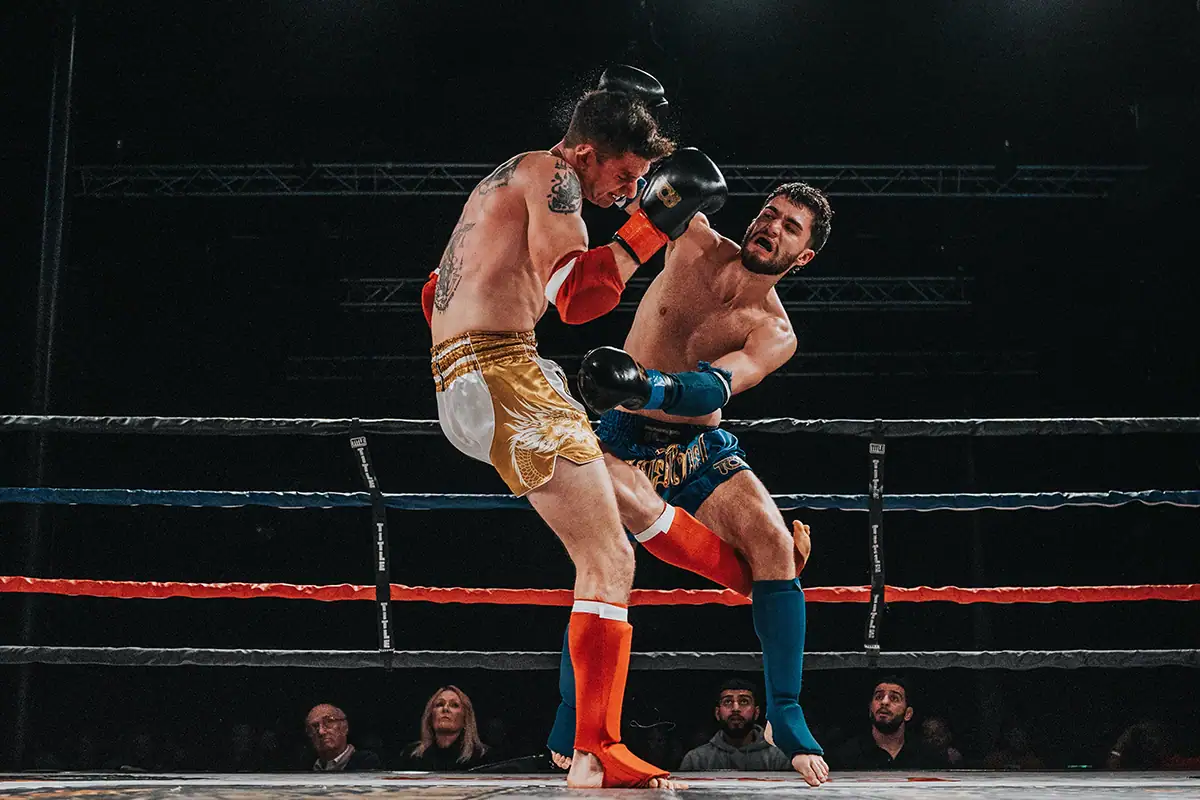 Two boxers compete in a ring during a low-light indoor sports event.