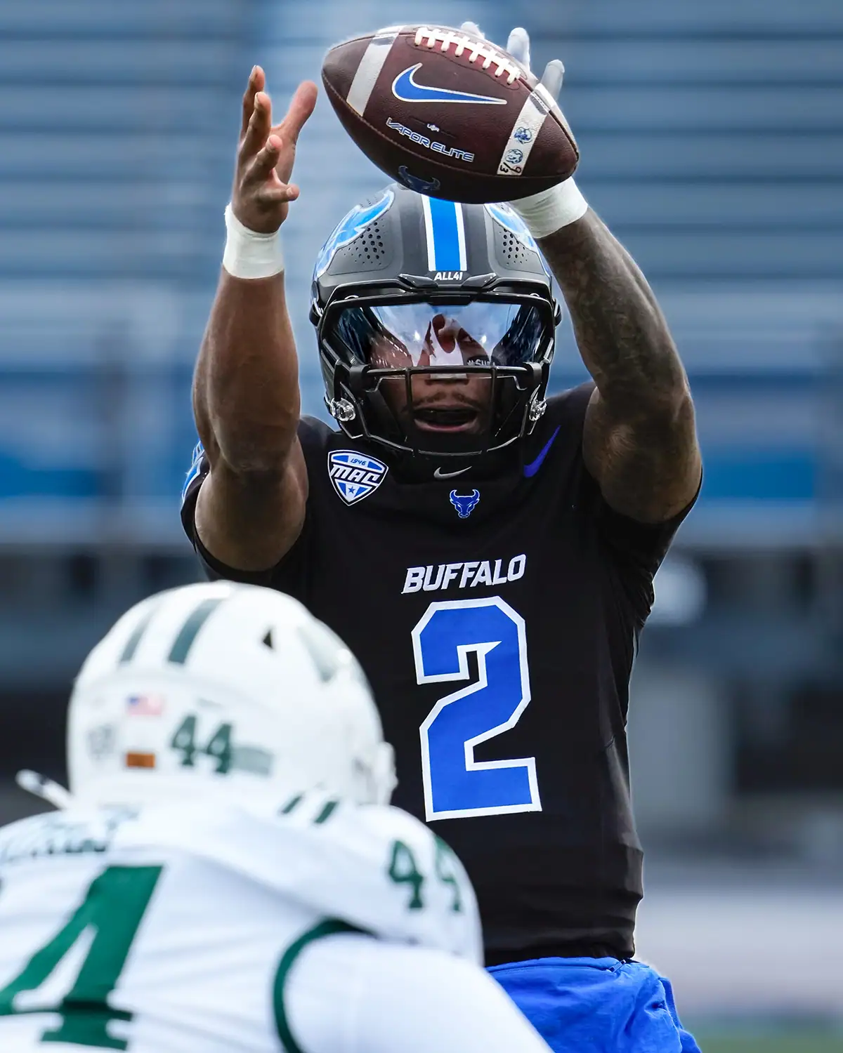 A football player reaches up for the ball during a peak-action moment in the game.