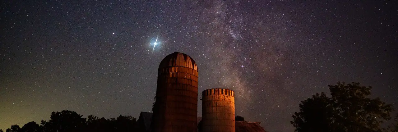 Milky Way rising above silos under a star-filled night sky.