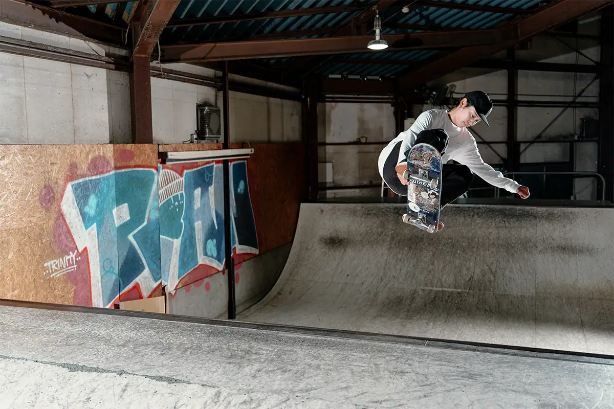 A skateboarder performs an aerial trick in a dim indoor skatepark.
