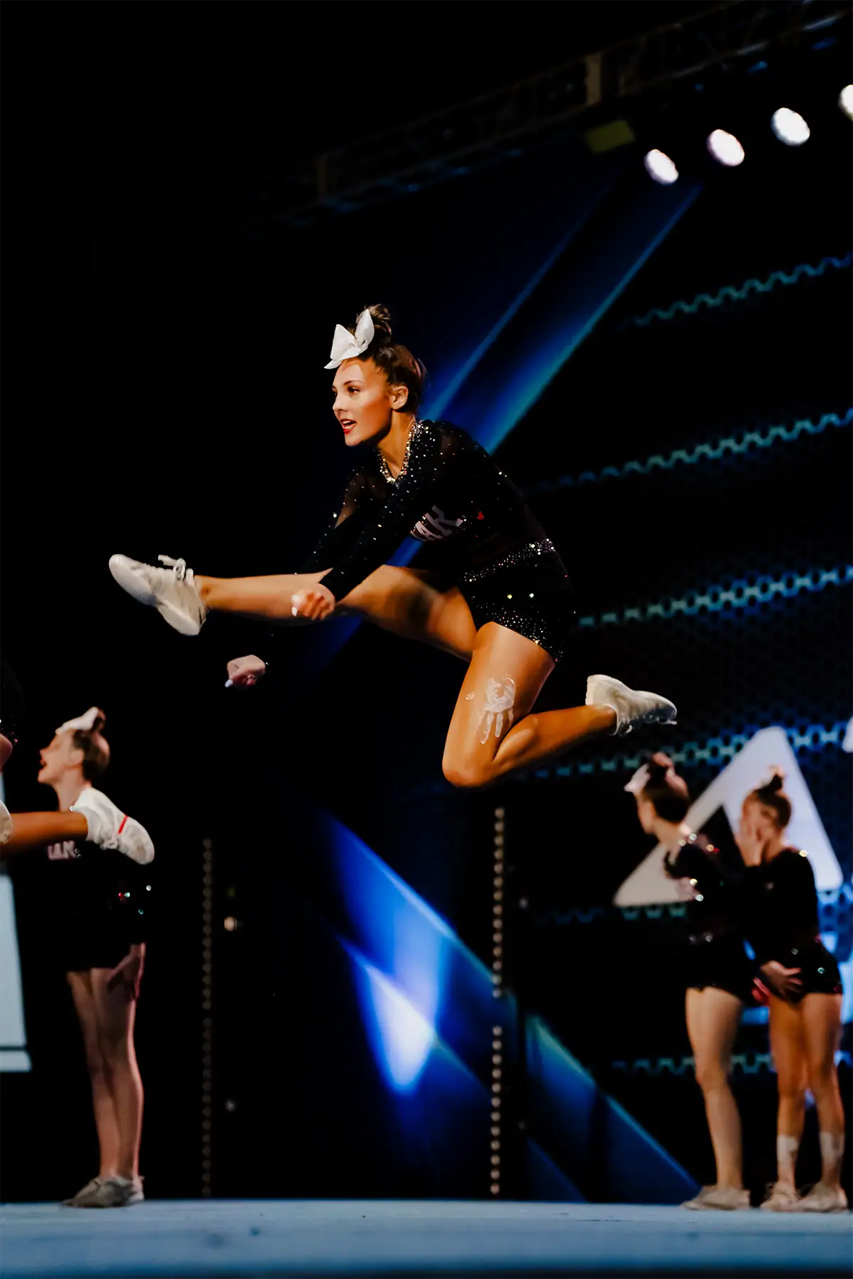 Indoor sports photography image of a cheerleader jumping under arena lighting.
