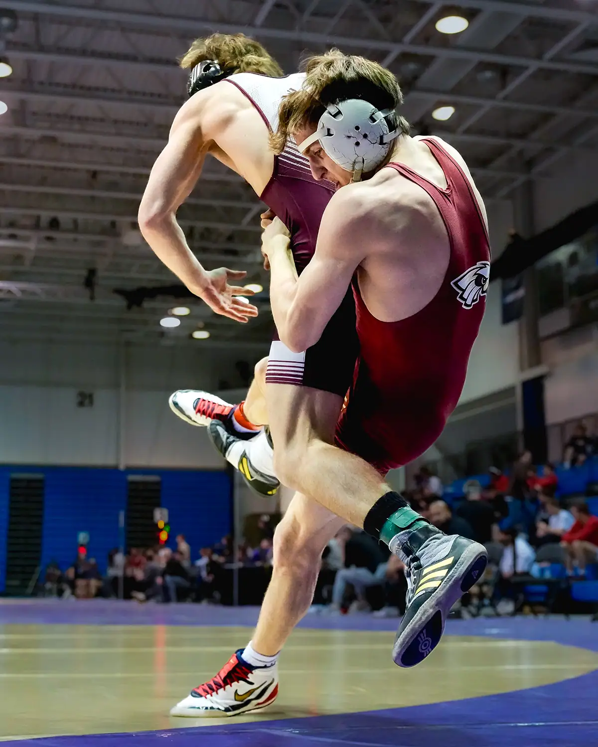 Two wrestlers compete during an indoor sports match under artificial lighting.