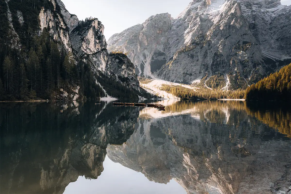 A calm mountain lake reflects cliffs, trees, and boats in clear light.