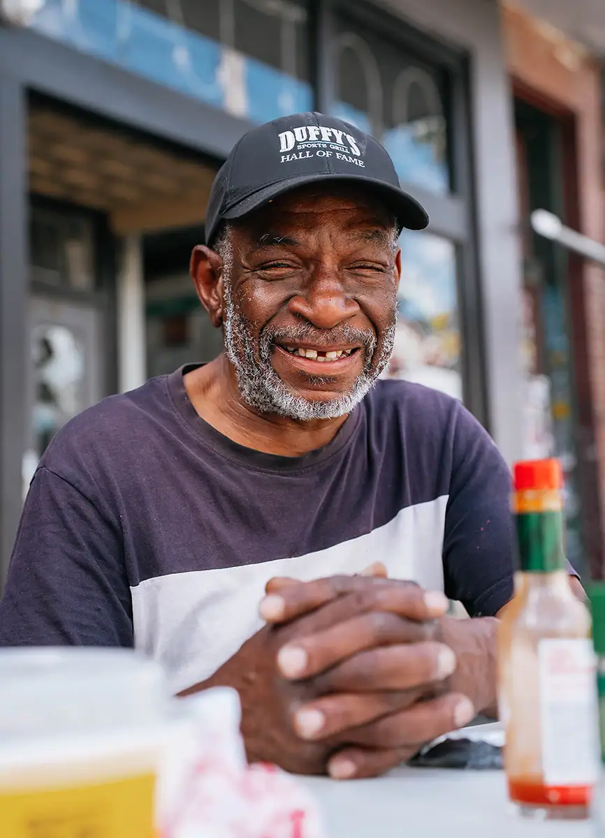 A guy wearing a Duffy's hat dining outside.