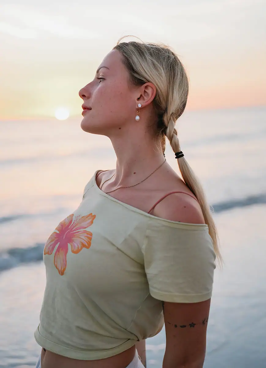 A woman on the beach at sunset with a flower shirt on.