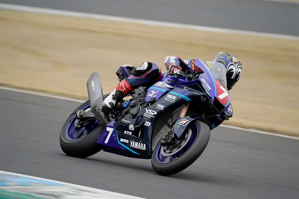 A motorcycle racer leans into a turn on a racetrack during a motorsports photography shoot.