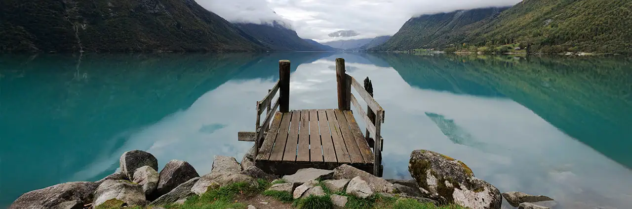 Wooden dock leading into a calm turquoise mountain lake surrounded by dramatic peaks.