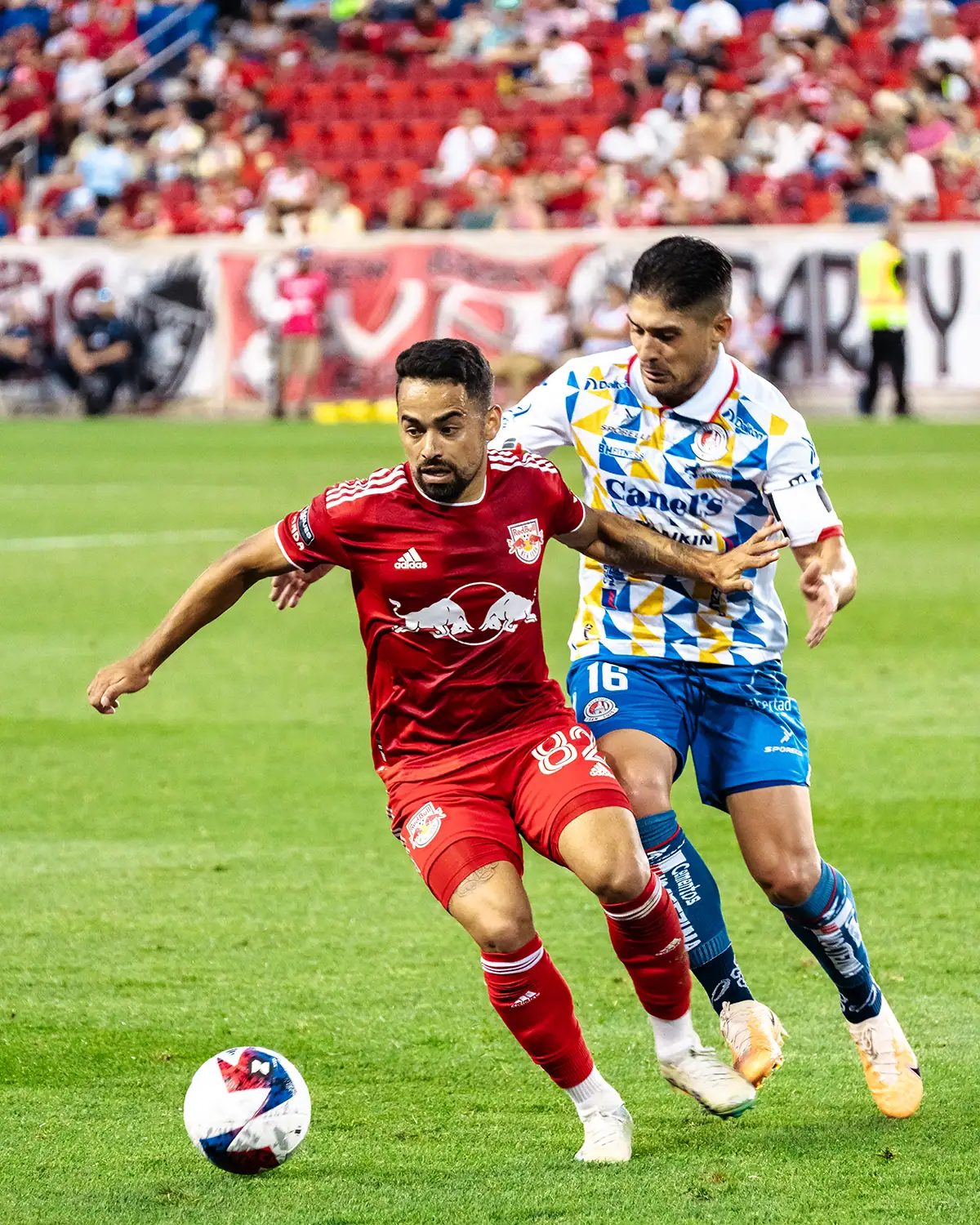 Two soccer players sprint toward the ball during a fast-moving match.