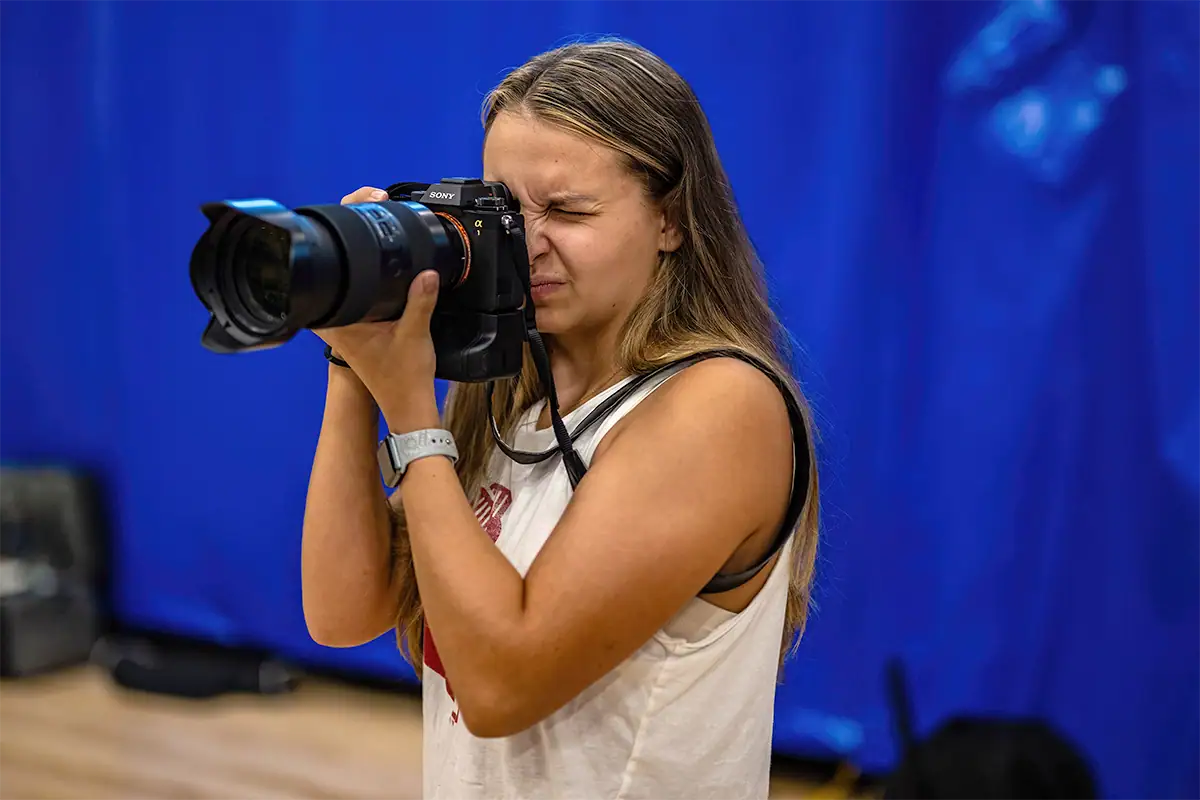 A photographer uses a mirrorless camera with a telephoto lens while preparing to capture indoor sports action.