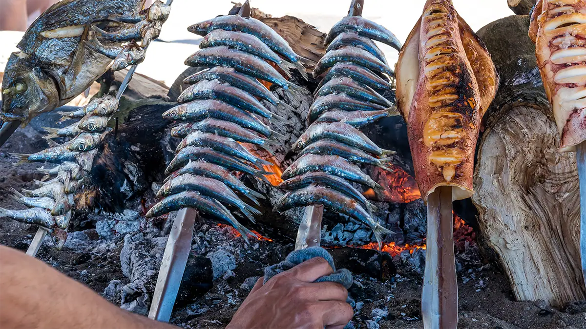 Sardines cooking over glowing embers along the Andalusian coast, photographed with the Tamron 35-100mm F2.8 travel photography lens.