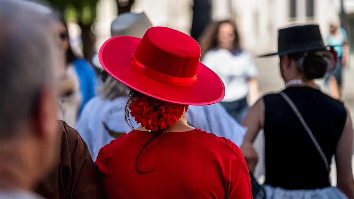 A person wearing a bright red sombrero cordob&eacute;s walks through an Andalusian street, photographed with the Tamron 35-100mm F2.8 travel photography lens.