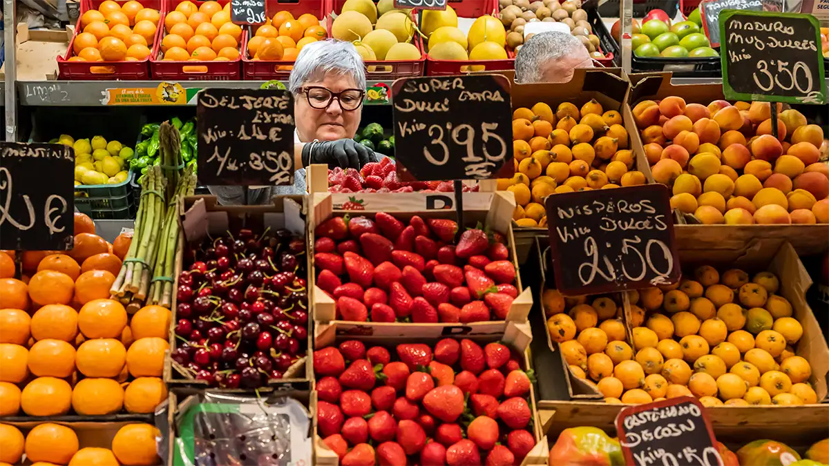 A vendor works behind colorful fruit displays at a market in Spain, photographed with the Tamron 35-100mm F2.8 travel photography lens.