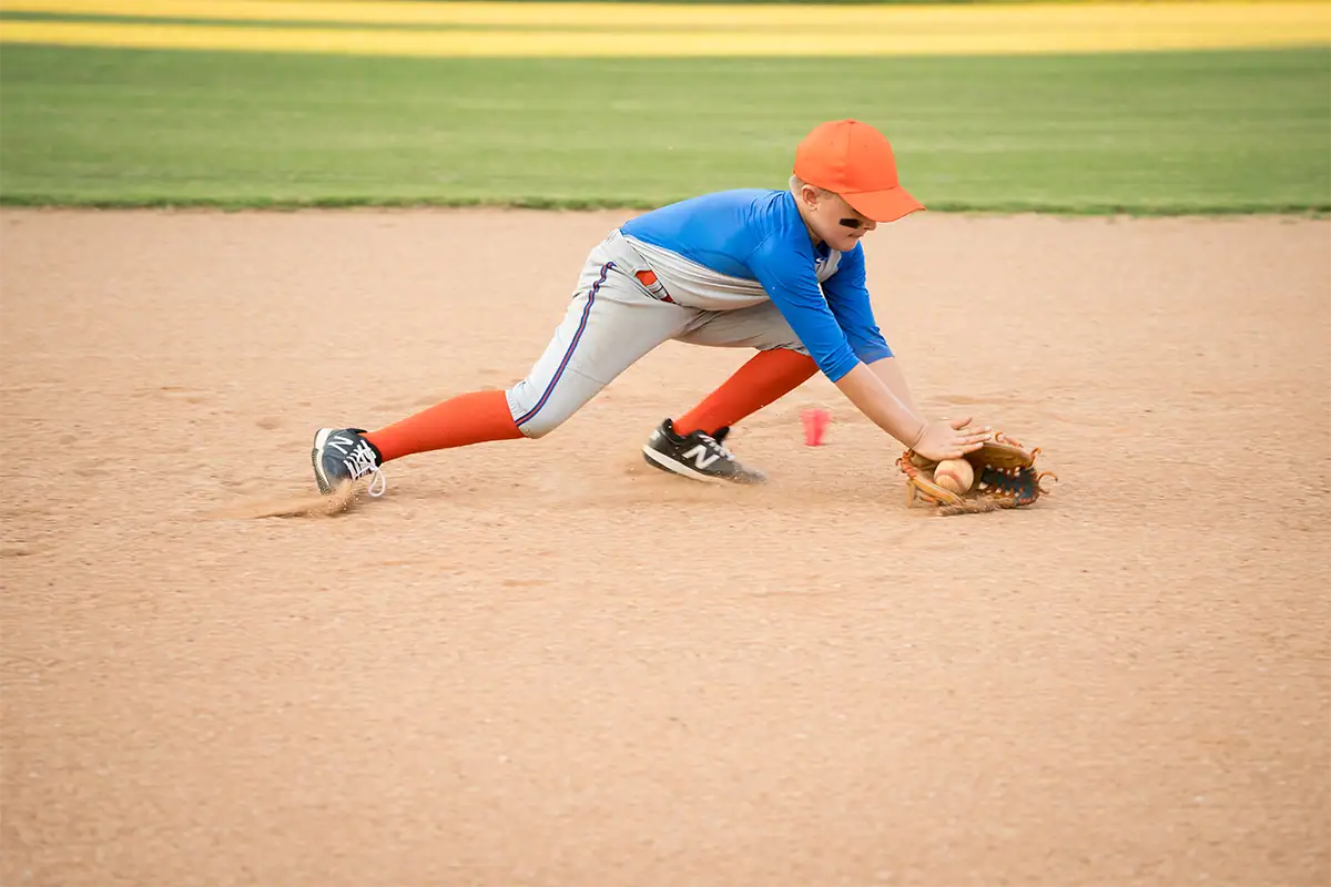 A young baseball player fields a ground ball during a youth sports game.