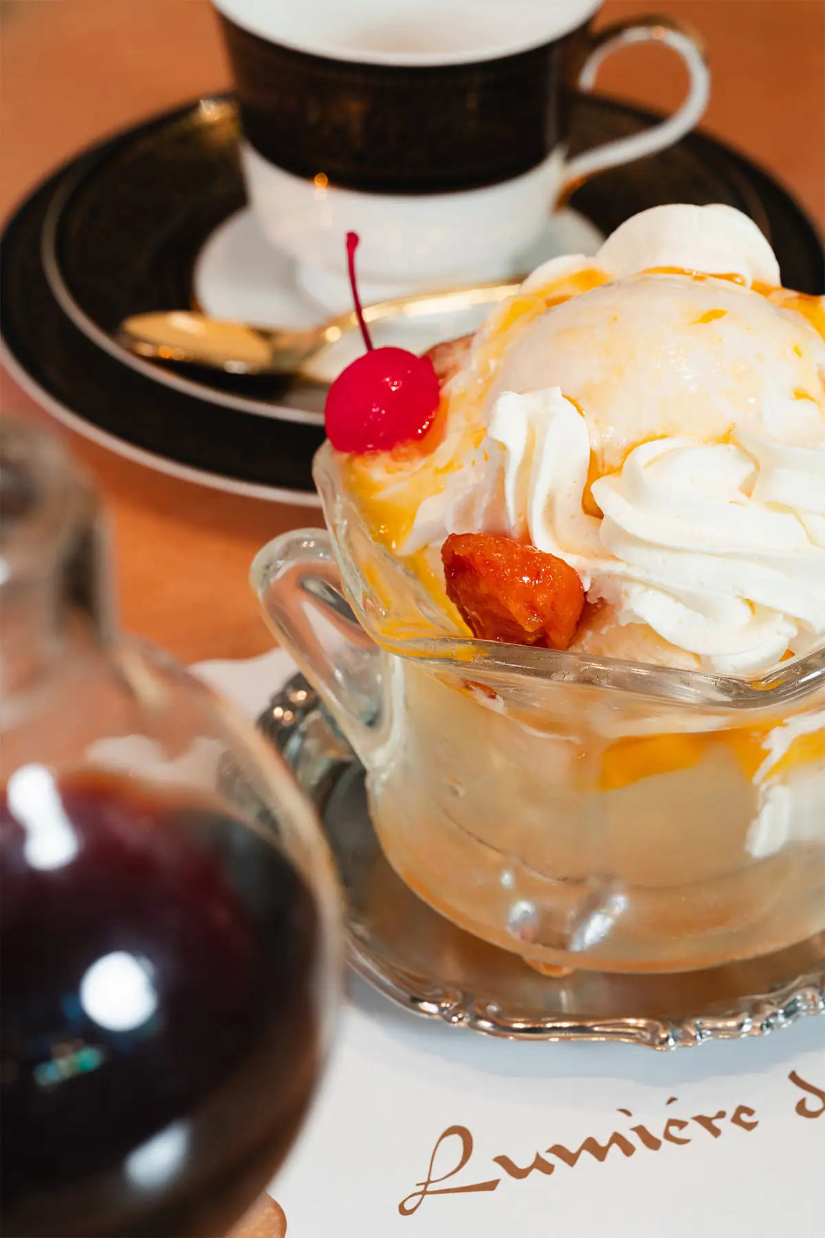 Fotografía de un postre de cafetería: helado con crema batida y una cereza en un plato de vidrio, con poca profundidad de campo.