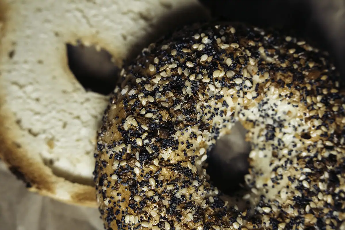 Foto en primer plano de comida de cafetería: un bagel «Everything» con sésamo y semillas de amapola, junto a un bagel simple cortado en rebanadas.