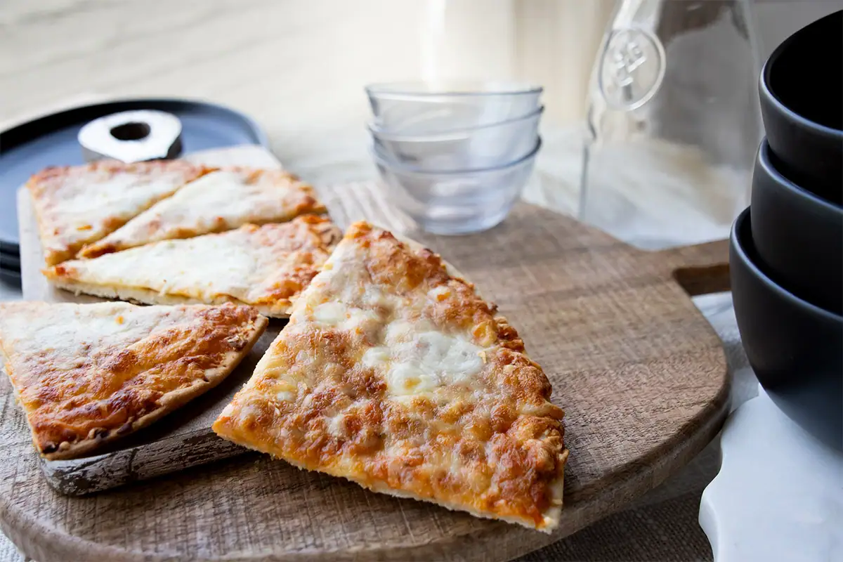 Fotografía gastronómica de una cafetería en la que se muestran rebanadas de pizza sobre una tabla de madera, con luz natural y una profundidad de campo suave, en el ambiente de una cafetería.