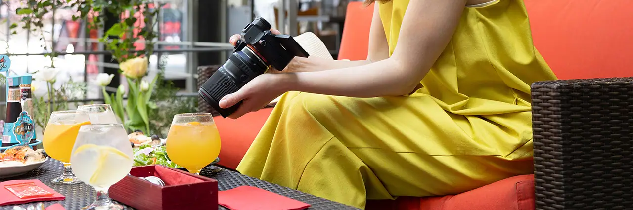 Photographer taking a cafe photo of drinks and food using a mirrorless camera in a coffee shop.