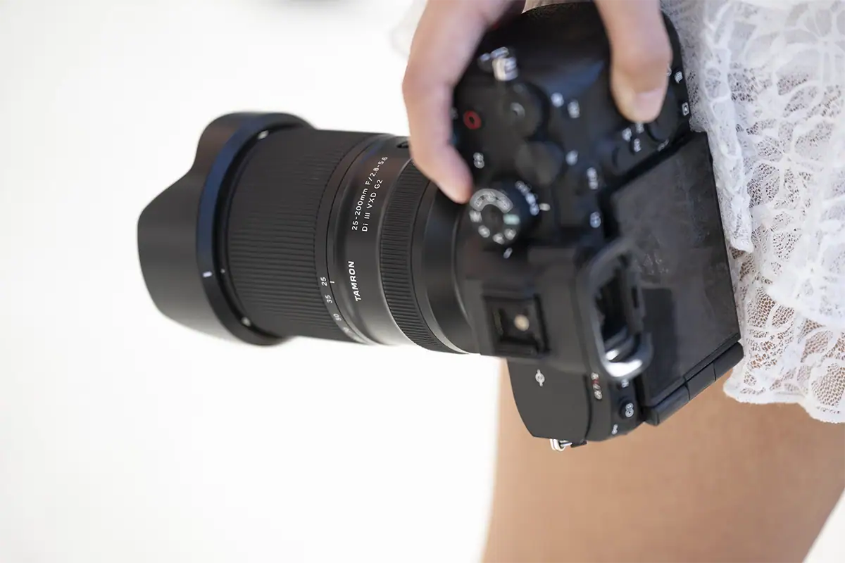Photographer holding a mirrorless camera fitted with a Tamron 25-200mm F/2.8-5.6 Di III VXD G2 zoom lens.