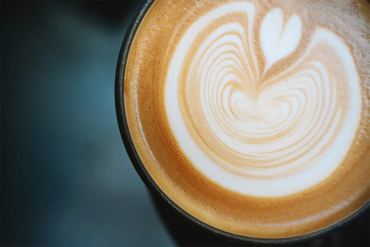 Fotografía de café en primer plano que muestra el arte del latte en una taza, con una textura cremosa y una suave profundidad de campo, en el ambiente de una cafetería.