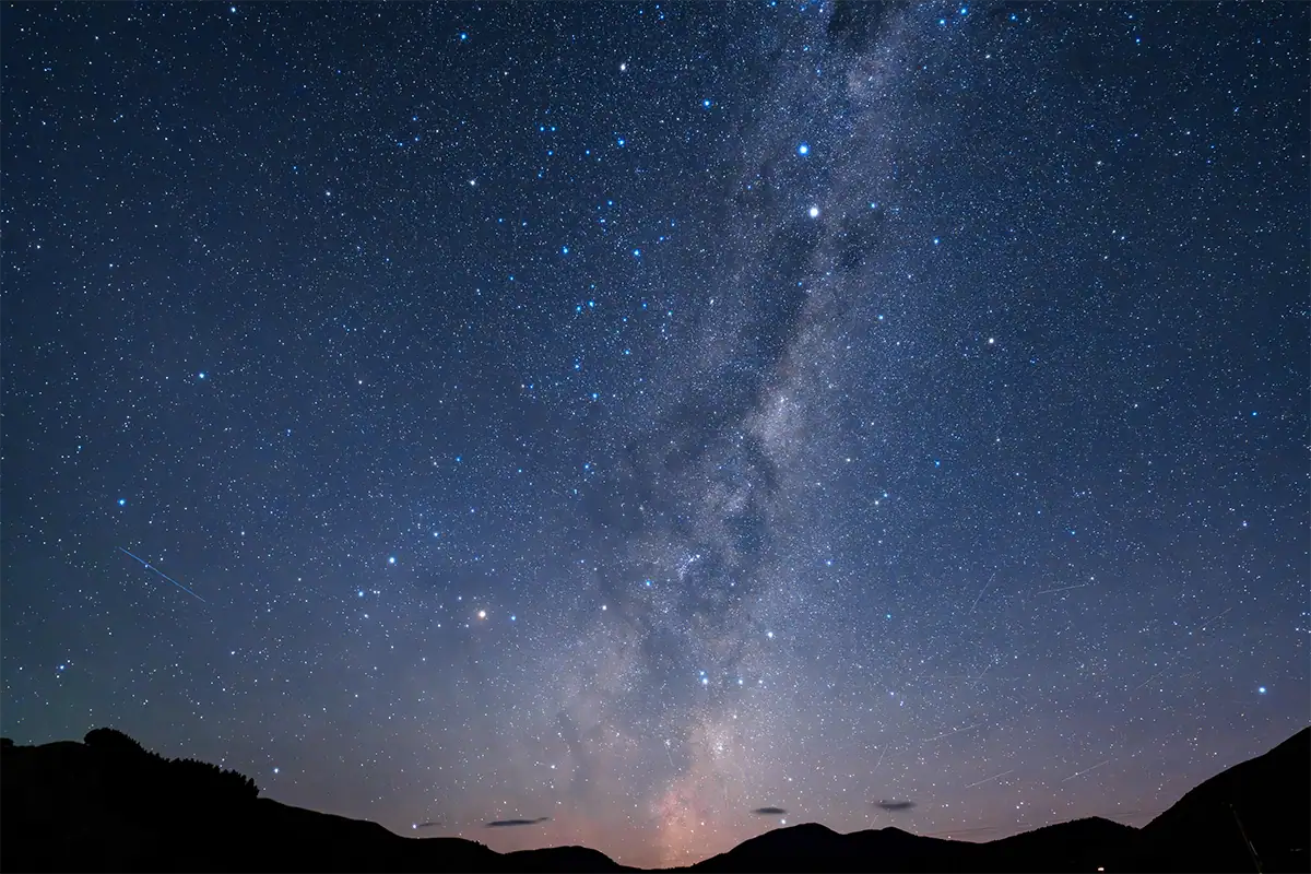 The Milky Way galactic core rising above a dark mountain horizon in a clear night sky.