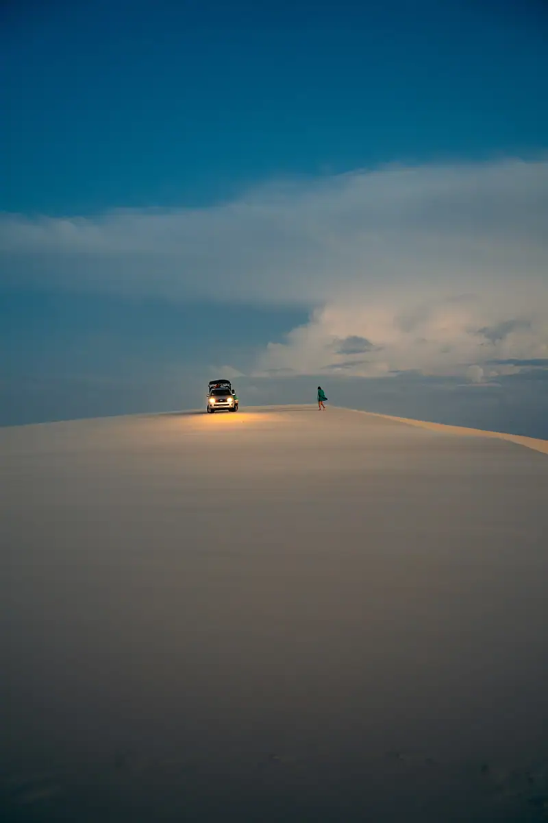 Foto noturna de um veículo com os faróis acesos, parado no topo de uma duna de areia
