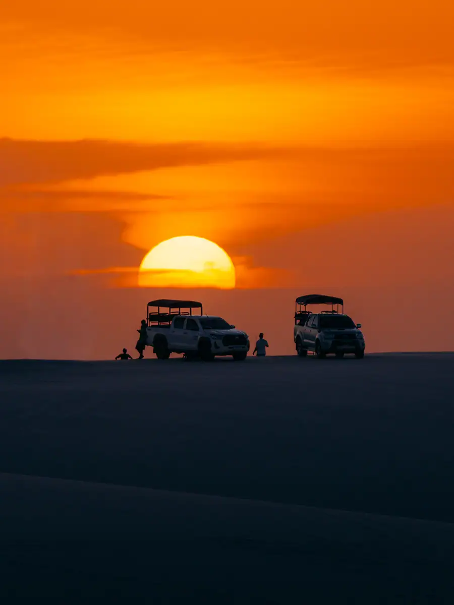 Dois veículos ao pôr do sol, com as silhuetas dos motoristas em pé no cume.