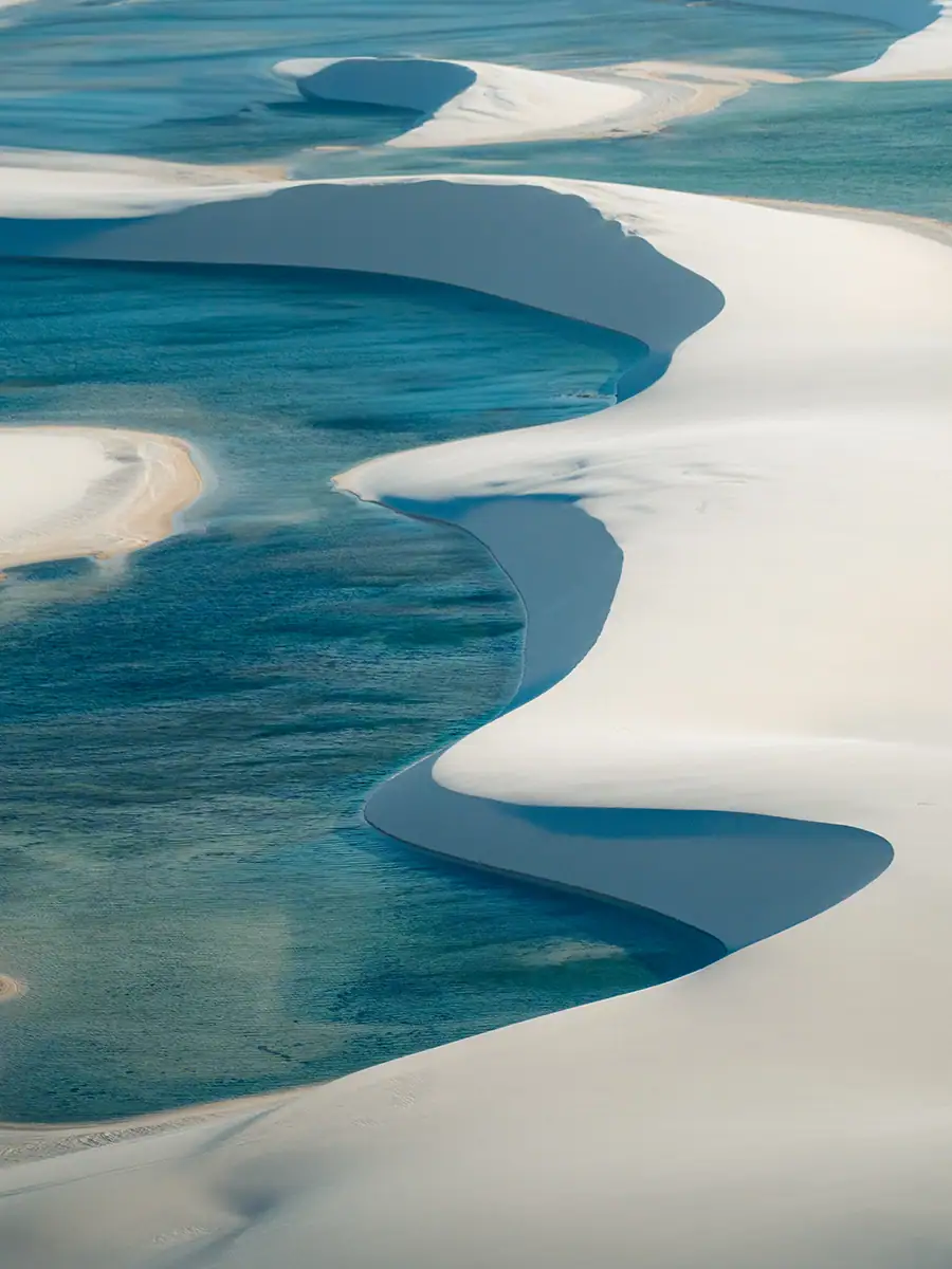 Um close-up de uma lagoa com areia branca, fotografado de um helicóptero com as portas abertas.