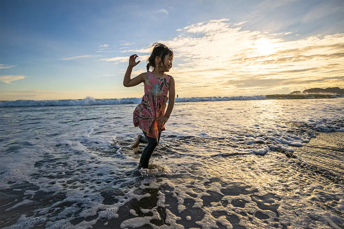 Child running through ocean waves at sunset, photographed with the Tamron 11-20mm lens for Canon RF mount.