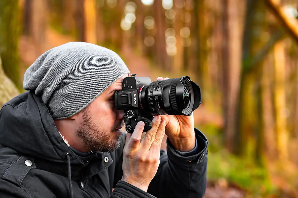 Photographer using a Tamron 12-20mm F2.8 lens on a Sony mirrorless camera in a sunlit forest.