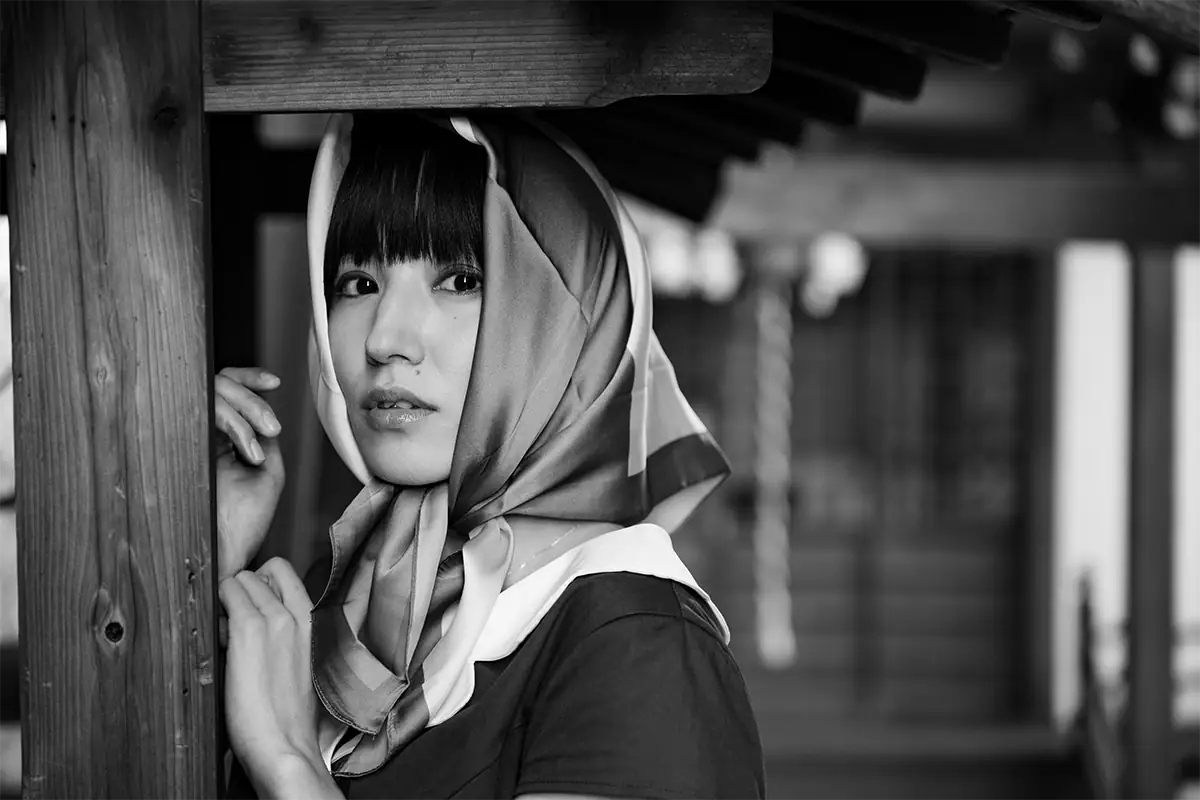 Black-and-white portrait of a woman wearing a patterned headscarf beside a wooden post, photographed with the Tamron 28-75mm for Nikon Z mount.