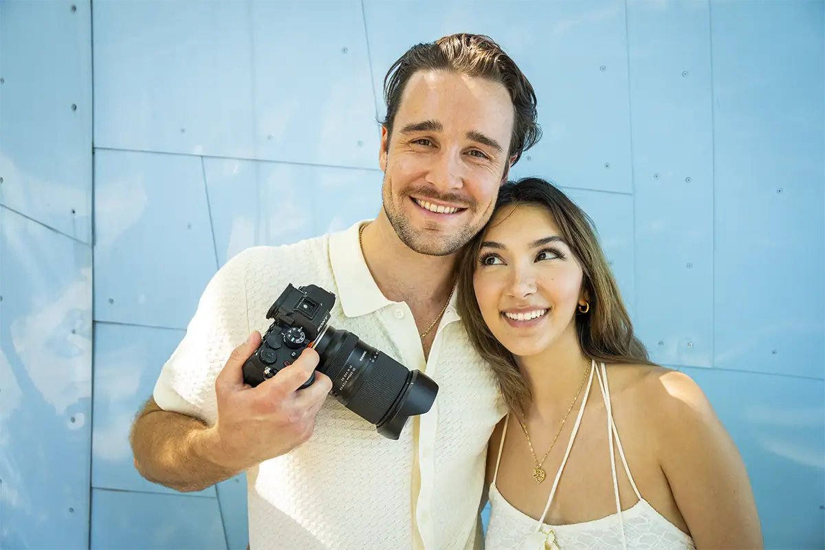 Smiling couple traveling with a mirrorless camera and Tamron zoom lens.