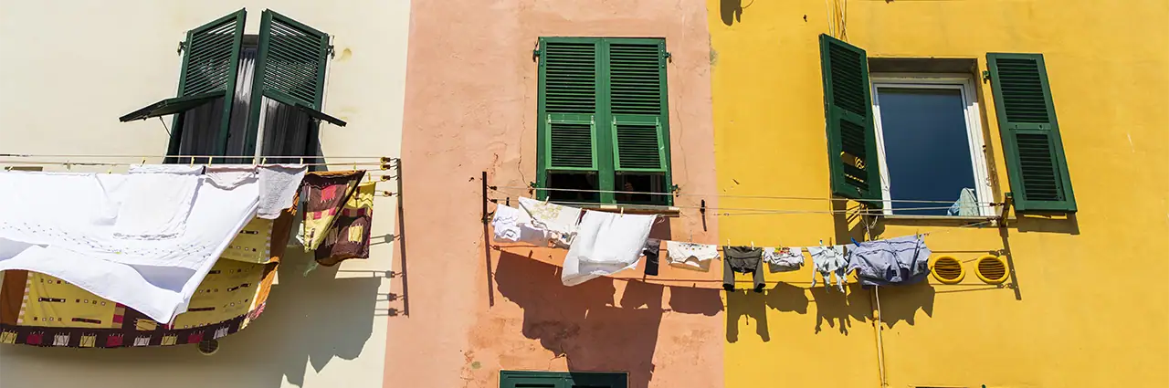 Colorful coastal buildings with green shutters and laundry hanging outside in bright sunlight.