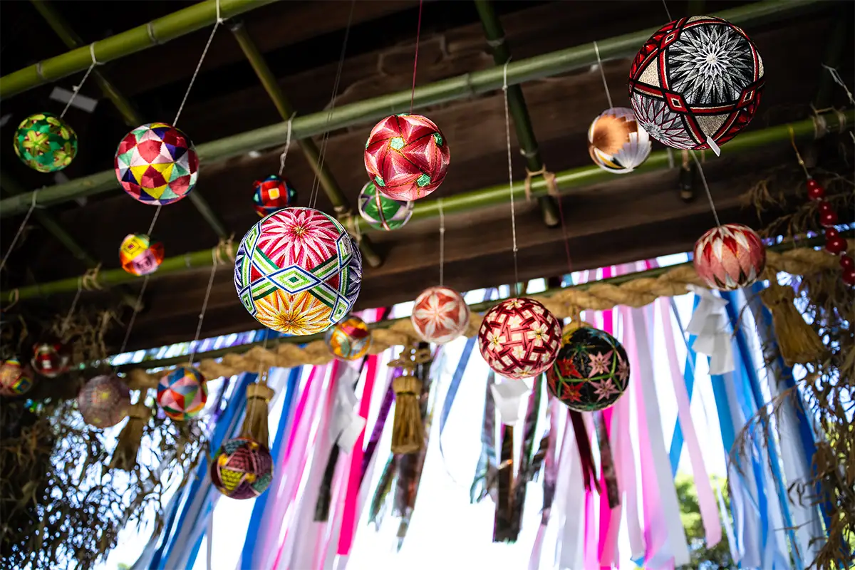 Colorful Japanese temari balls hanging from bamboo above bright decorative ribbons.
