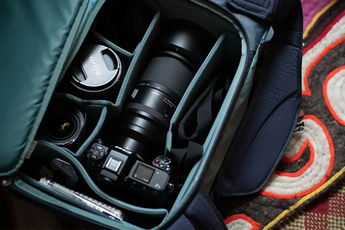 Open camera bag with Tamron lenses and camera gear organized in padded divider compartments.