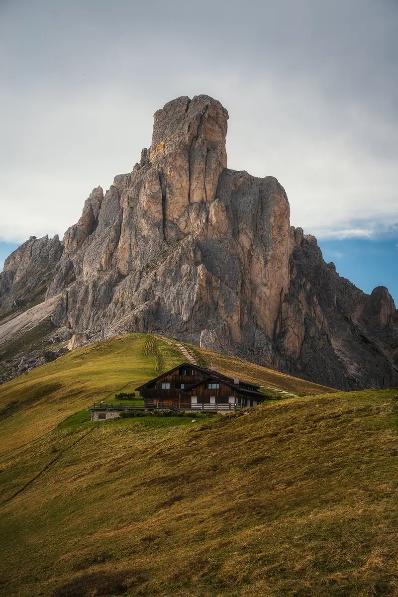 A foreground meadow leads to the hut, which then leads to the towering peak in the background