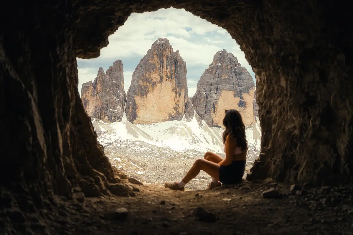 A cave is a natural frame for the person sitting and the mountains in the distance