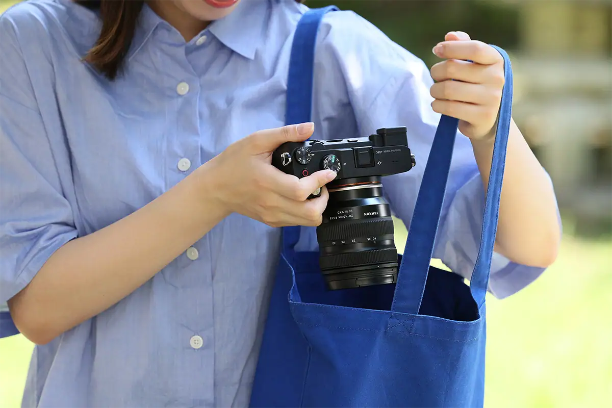 Fotógrafo colocando uma câmera sem espelho com uma lente zoom padrão compacta da Tamron dentro de uma pequena bolsa azul para facilitar o transporte no dia a dia.
