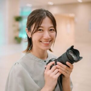 A fotógrafa Hiroko Ishii sorri enquanto segura uma câmera e uma lente zoom.