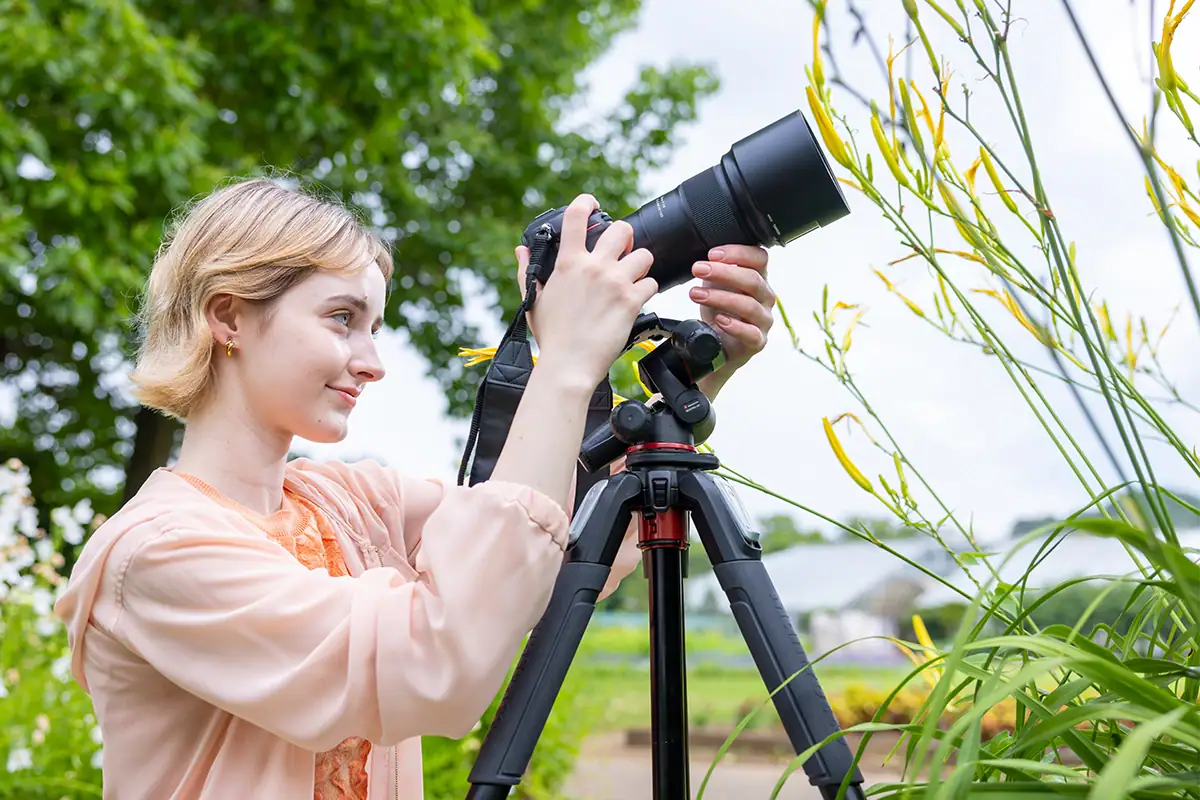 Fotógrafo usando uma câmera e um tripé para gravar um vídeo em close-up de plantas em flor ao ar livre.