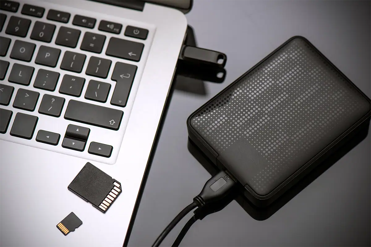 Portable external hard drive connected to a laptop with SD and microSD memory cards for photography file backup and storage.