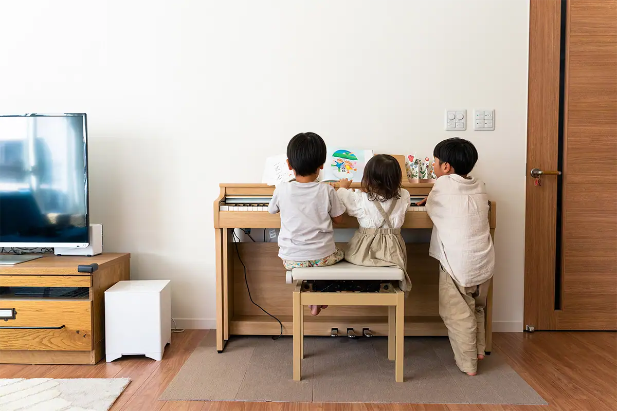 Três crianças reunidas ao redor de um piano na sala de estar, fotografadas com uma lente zoom padrão para capturar a atividade e o espaço ao redor.