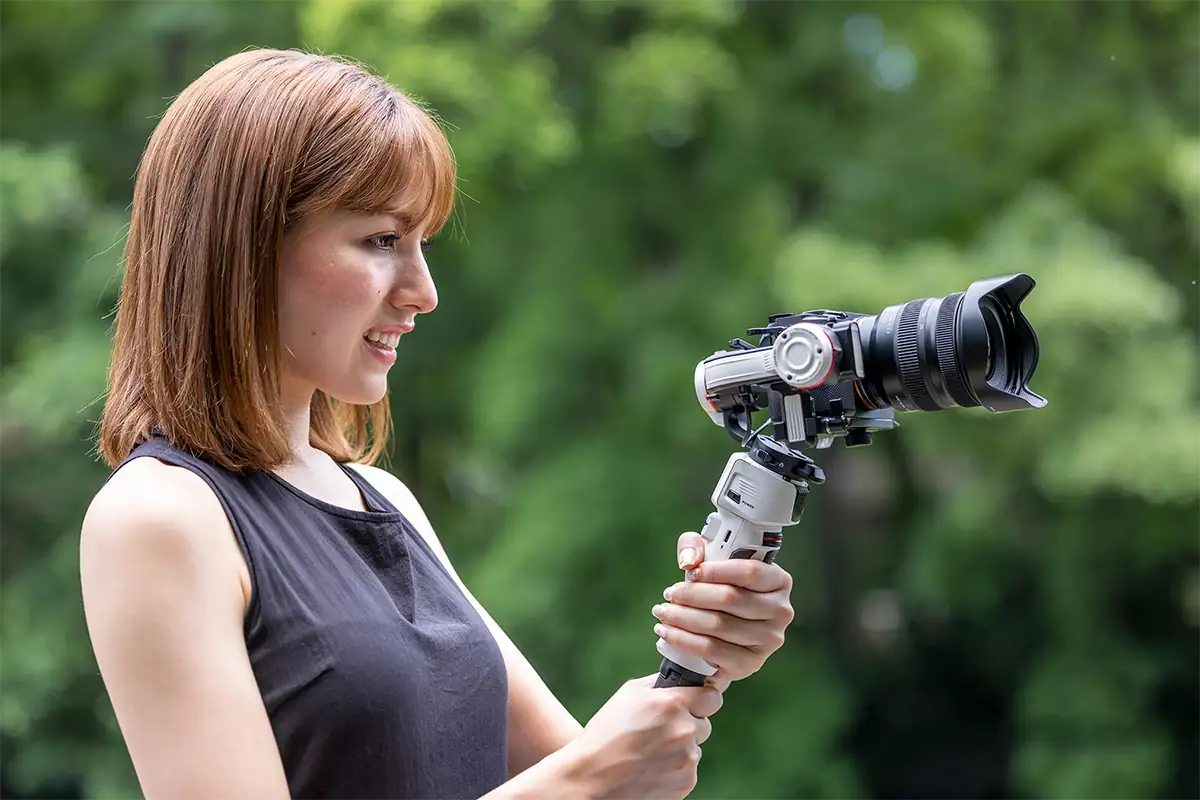 Criador de conteúdo segurando uma câmera sem espelho com uma lente zoom padrão acoplada a um gimbal portátil ao ar livre.